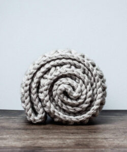 Mini bean stitch crochet cowl rolled up on wooden table against white/grey wall