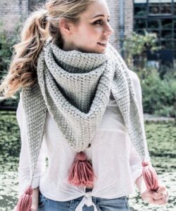 Oversized crochet triangle scarf in grey with pink tassels, worn by a canal