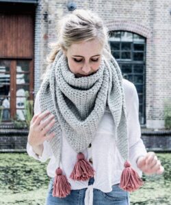 Oversized crochet triangle scarf in grey with pink tassels, worn by a canal